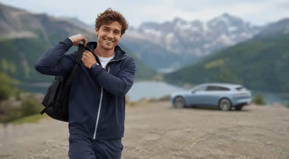 Person mit Rucksack in den Alpen, im Hintergrund ein hellblauer Elektro-Kombi
